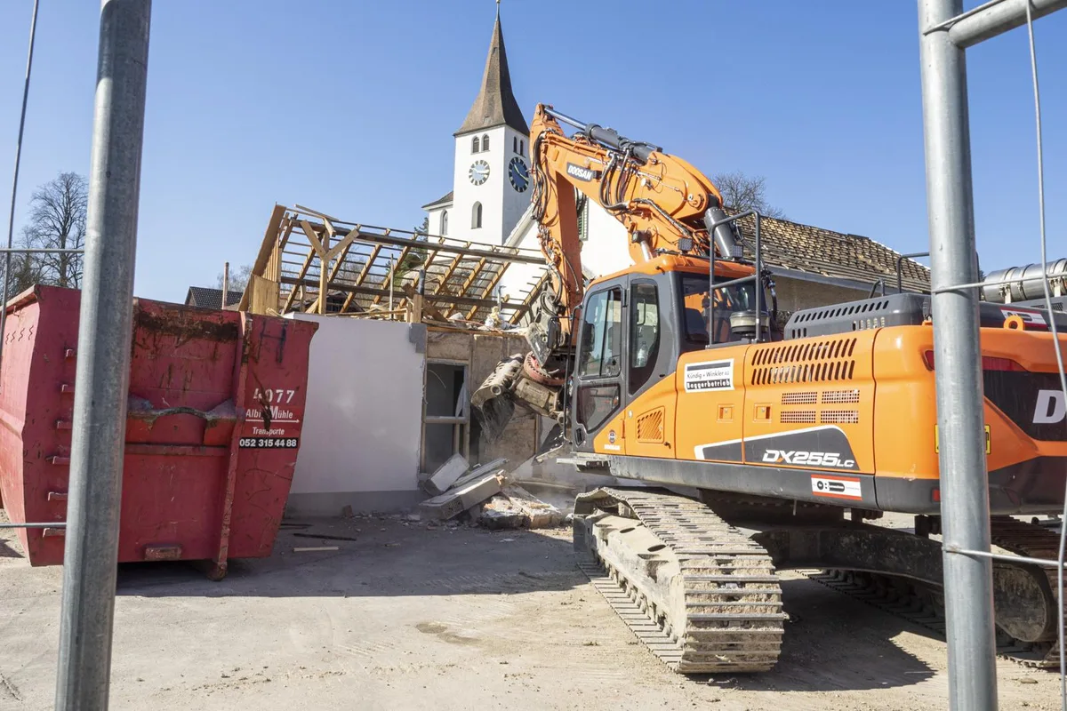 wila_abriss_kaeserei06_preview Hier rückt ein Bagger der Wilemer Käserei zu Leibe., Das alte Gebäude muss dem Neubauprojekt Zentrum Wila weichen., Der Bagger-Greifer lässt den Verputz bröckeln und die Backsteine zerbersten., «Ade, Chäsi!», meinte eine Anwohnerin, die das Spektakel vom Balkon aus verfolgte.