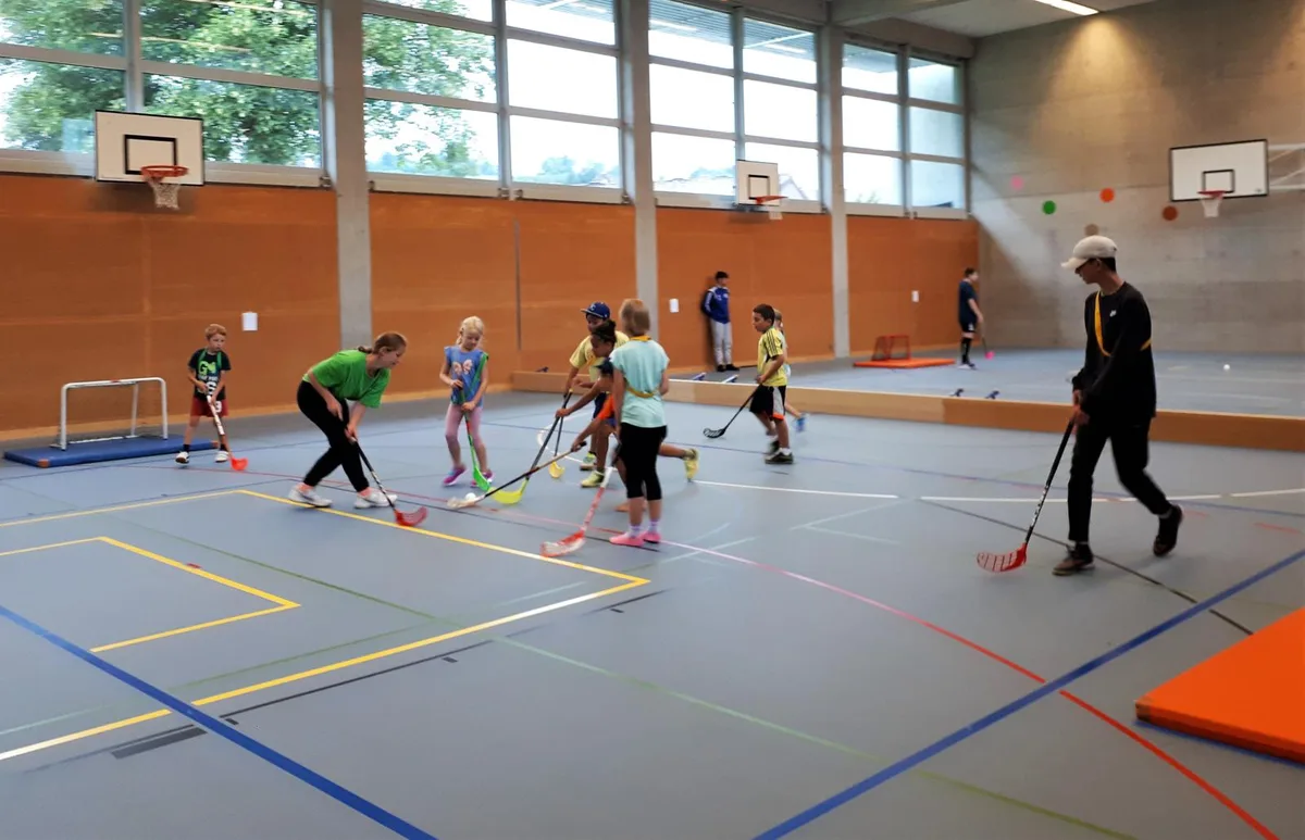 20200724_092550-1_preview_0 Beim Unihockey ging es in der Unterstufengruppe zur Sache., Draussen erwartete die älteren Teilnehmer ein Geschicklichkeitsparcours., Dort konnten sie ihre Fertigkeiten mit Schläger und Ball unter Beweis stellen., Die beiden Co-Projektleiter Ryan Hamilton und Angela Brüngger sind mit dem Ferienplausch zufrieden., Nach so viel Bewegung ist eine Znünipause angebracht.