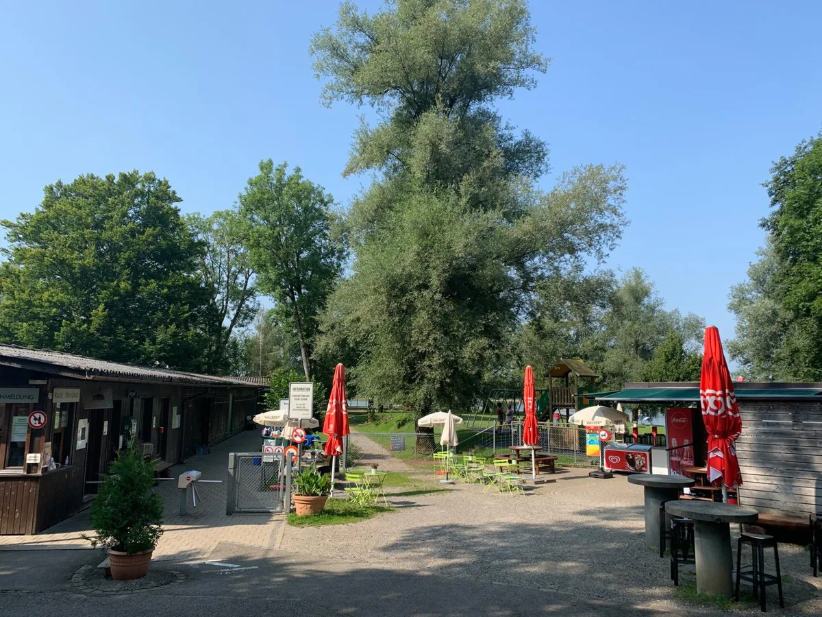 Der Eingang zum Strandbad Auslikon dürfte in drei Jahren völlig anders aussehen., Auch die Gebäude mit den Einzelkabinen werden verschwinden., So sind die Gebäude heute verteilt: Eingang, Garderoben, Kiosk und WC sind aufgeteilt., So könnte das neue, zentrale Infrastrukturgebäude in der Badi platziert werden., Diese Luftaufnahme der Badi Auslikon stammt aus dem Jahr 1946. , Zum Badibetrieb in den 1930er Jahren gehörte ein Sprungtrum., Für den Bau der Badi Auslikon musste der Bach verlegt werden, wie dieser Plan von 1926 zeigt., Badibetrieb im Jahr 1972., Das alte Kassenhaus - hier eine Aufnahme von 1958 - brannte 1987 ab. , In den ersten Jahren nach Eröffnung des Strandbades Auslikon 1931 musste nur am Wochenende Eintritt gezahlt werden. , Das neue Infrastrukturgebäude dürfte mehr in den hinteren Bereich der Badi zu liegen kommen., 1949 wurden für das Bad 63'500 Franken bewilligt. Es wurden 40 Kabinen erstellt. Im jenem Sommer wurden 15'000 Gäste gezählt. , Die öffentlichen WCs werden abgebrochen und verlegt., Die langen Holzbaracken werden Ende 2023 abgerissen., Die Tage des heutigen Kassagebäudes sind nun auch gezählt., Der Kiosk soll vom Bach weg verlegt werden., Der Campingplatz wird 2023 aufgehoben., Auch in der umgebauten Badi soll es wieder einen Spielplatz geben.