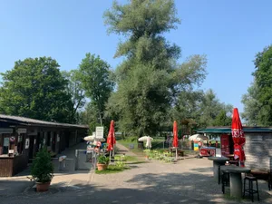 200821_badi_auslikon_7_cb_preview Der Eingang zum Strandbad Auslikon dürfte in drei Jahren völlig anders aussehen., Auch die Gebäude mit den Einzelkabinen werden verschwinden., So sind die Gebäude heute verteilt: Eingang, Garderoben, Kiosk und WC sind aufgeteilt., So könnte das neue, zentrale Infrastrukturgebäude in der Badi platziert werden., Diese Luftaufnahme der Badi Auslikon stammt aus dem Jahr 1946. , Zum Badibetrieb in den 1930er Jahren gehörte ein Sprungtrum., Für den Bau der Badi Auslikon musste der Bach verlegt werden, wie dieser Plan von 1926 zeigt., Badibetrieb im Jahr 1972., Das alte Kassenhaus - hier eine Aufnahme von 1958 - brannte 1987 ab. , In den ersten Jahren nach Eröffnung des Strandbades Auslikon 1931 musste nur am Wochenende Eintritt gezahlt werden. , Das neue Infrastrukturgebäude dürfte mehr in den hinteren Bereich der Badi zu liegen kommen., 1949 wurden für das Bad 63'500 Franken bewilligt. Es wurden 40 Kabinen erstellt. Im jenem Sommer wurden 15'000 Gäste gezählt. , Die öffentlichen WCs werden abgebrochen und verlegt., Die langen Holzbaracken werden Ende 2023 abgerissen., Die Tage des heutigen Kassagebäudes sind nun auch gezählt., Der Kiosk soll vom Bach weg verlegt werden., Der Campingplatz wird 2023 aufgehoben., Auch in der umgebauten Badi soll es wieder einen Spielplatz geben.