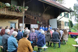 210926_erntedankzell_1_bes_preview Die Besucher lauschen den Klängen der «Zürcher Jodelfründe»., Pfarrer Jens Liedtke (Mitte) begrüsst die Anwesenden., Gastgeber und Landwirt Ruedi Furrer darf seinen Hof vorstellen., Besucherinnen decken sich nach dem Gottesdienst am Gabentisch ein., Nach der Feier verpflegen sich die Besucher am Apéro.
