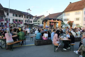 srf2_preview Viele Besucherinnen und Besucher waren schon vor Drehbeginn vor Ort., Einlass erhielt man nur mit einem Covid-Zertifikat. Es bildete sich vor dem Eingang eine Schlange., In den Anlass integriert war auch das Forellenfest des Verkehrsvereins., Dieser hatte ein eigenes Festzelt auf dem Gelände., Die Teller sind bereits vorbereitet., Die erste Forelle des Abends landet auf dem Teller., Geübt werden Gräten und Kopf entfernt..., ... entsorgt., Wer keinen Fisch mochte, durfte sich in den Restaurants oder am Grillstand verpflegen., Einlass gab es für maximal 1500 Personen., Letzte Vorkehrungen vor den Dreharbeiten.