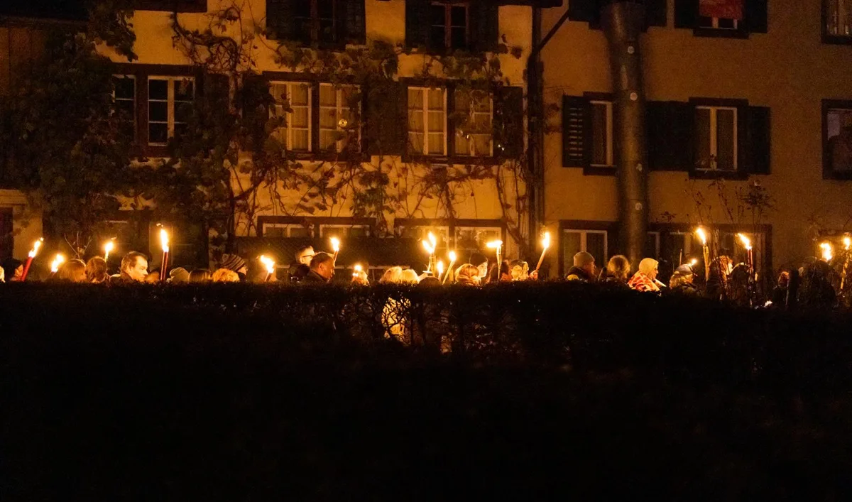 hinwil_16112021_coronademo_crm_7_preview Fackeln erleuchten die dunkle Nachtluft., Die Massnahmen-Kritiker sind mit Nationalflaggen, Plakaten und Kuhglocken ausgestattet., Der Marsch beginnt: Die Demonstranten ziehen Richtung Überbauung Mosaik., Mitten auf dem Platz beim Hirschen Hinwil legen die Trychler ihre Glocken nieder., Während des Umzuges jubeln die Menschen lauthals., Der Bus kann sich gerade noch so an den Demonstrierenden vorbeizwängen., Die Menschen ziehen weiter auf der rechten Spur. Die Polizei markiert Präsenz.