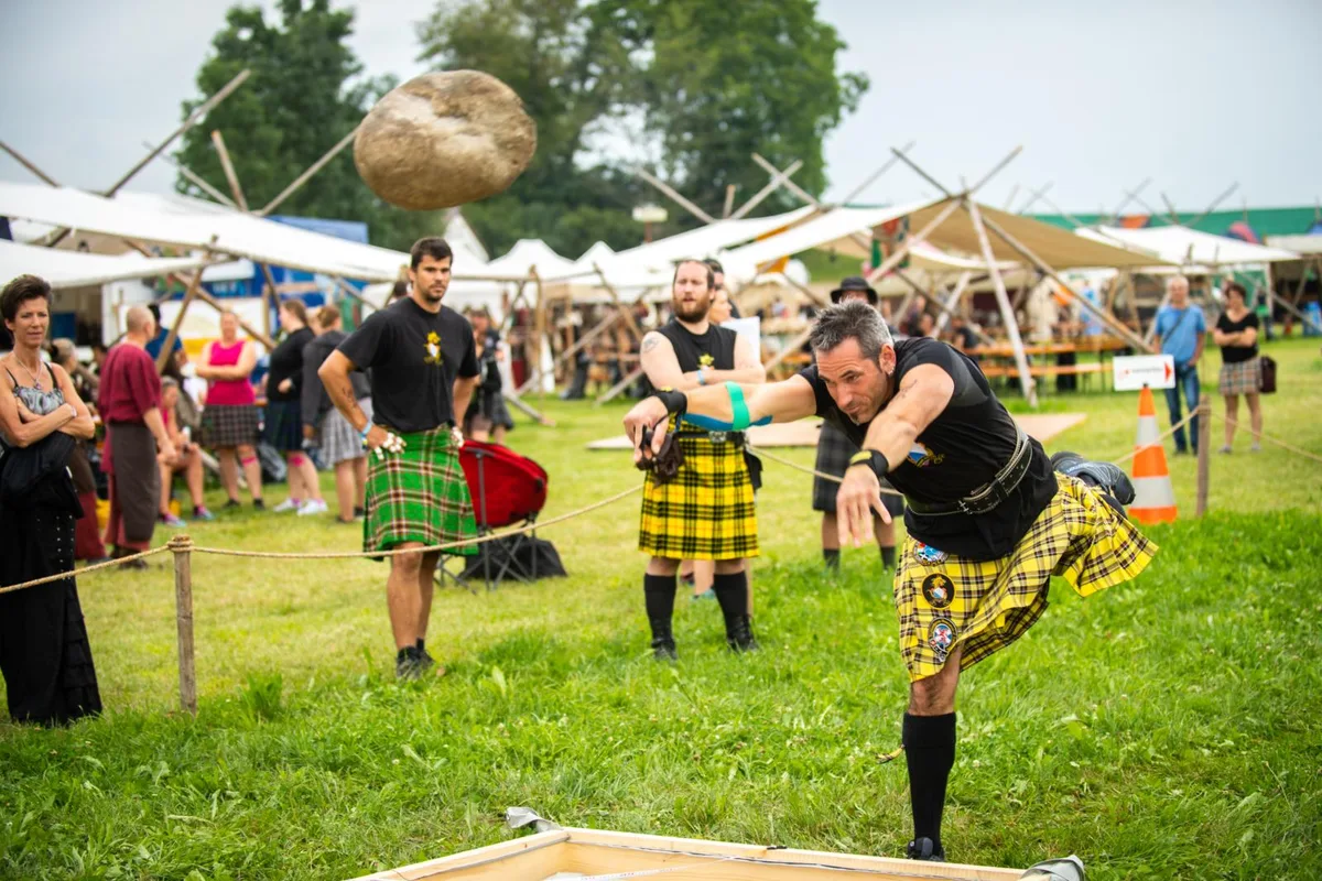 Ein Mann im Schottenrock wuchtet einen Stein an den Highland Games.