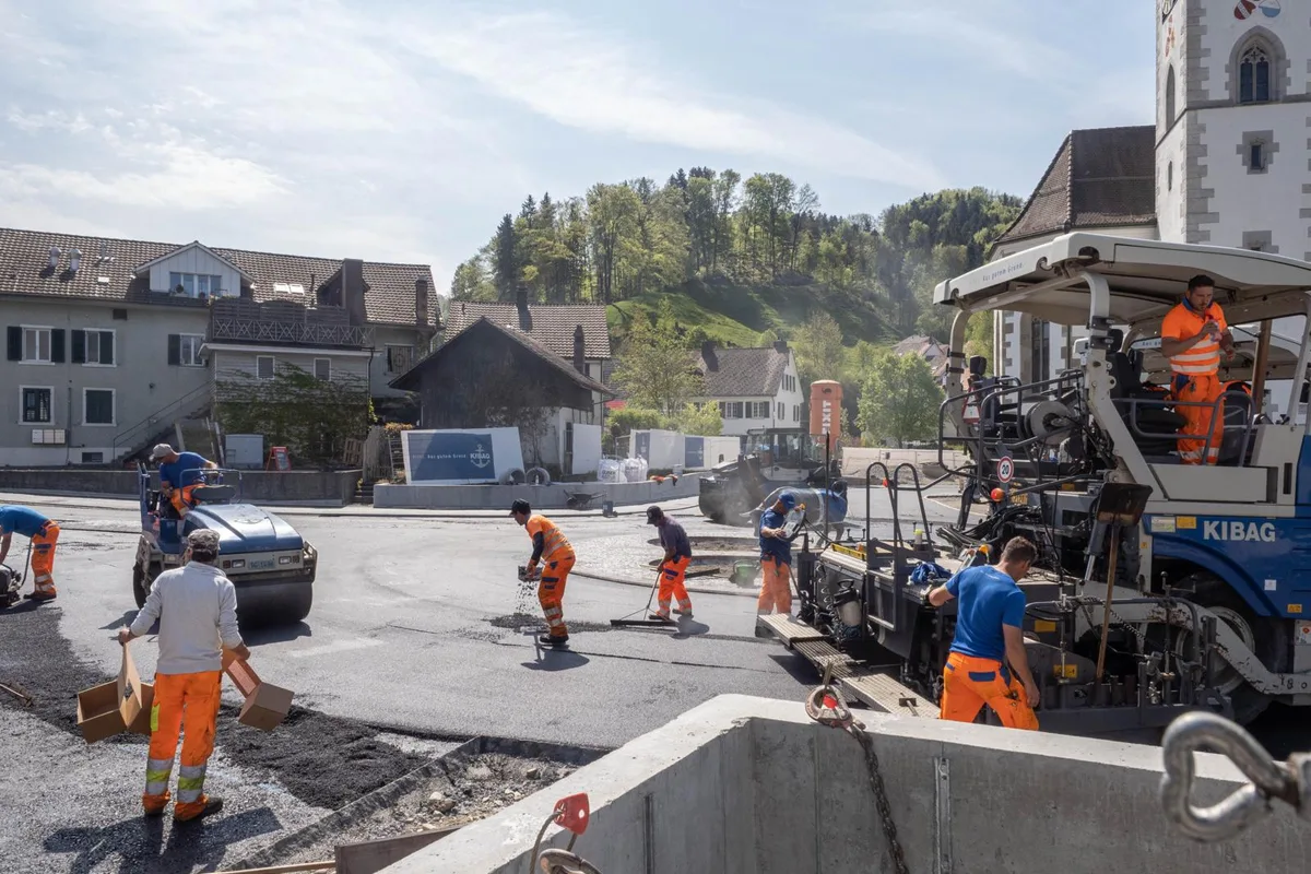 Beim neuen Kreisel in Turbenthal wird derzeit die Strasse asphaltiert., Für die Arbeiten sind verschiedene Maschinen im Einsatz., Wegen der Vollsperrung kann der Belag in einem Guss erfolgen., Das schnelle Voranschreiten freut die Verantwortlichen. Unter ihnen Tiefbauvorsteher Heinz M. Schwyter (rechts hinten).