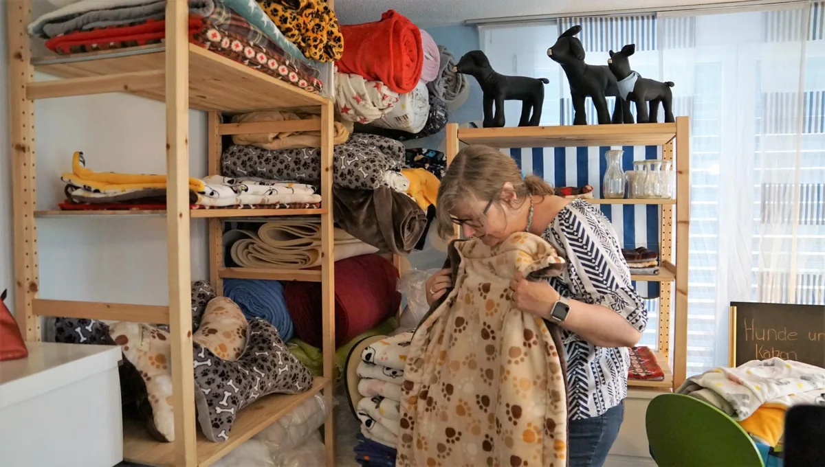 Claudia Wullschläger steht in ihrem Büro. Auf dem Gestell hinter ihr erkennt man viele Hundedecken. Sie hält eine Decke in der Hand.