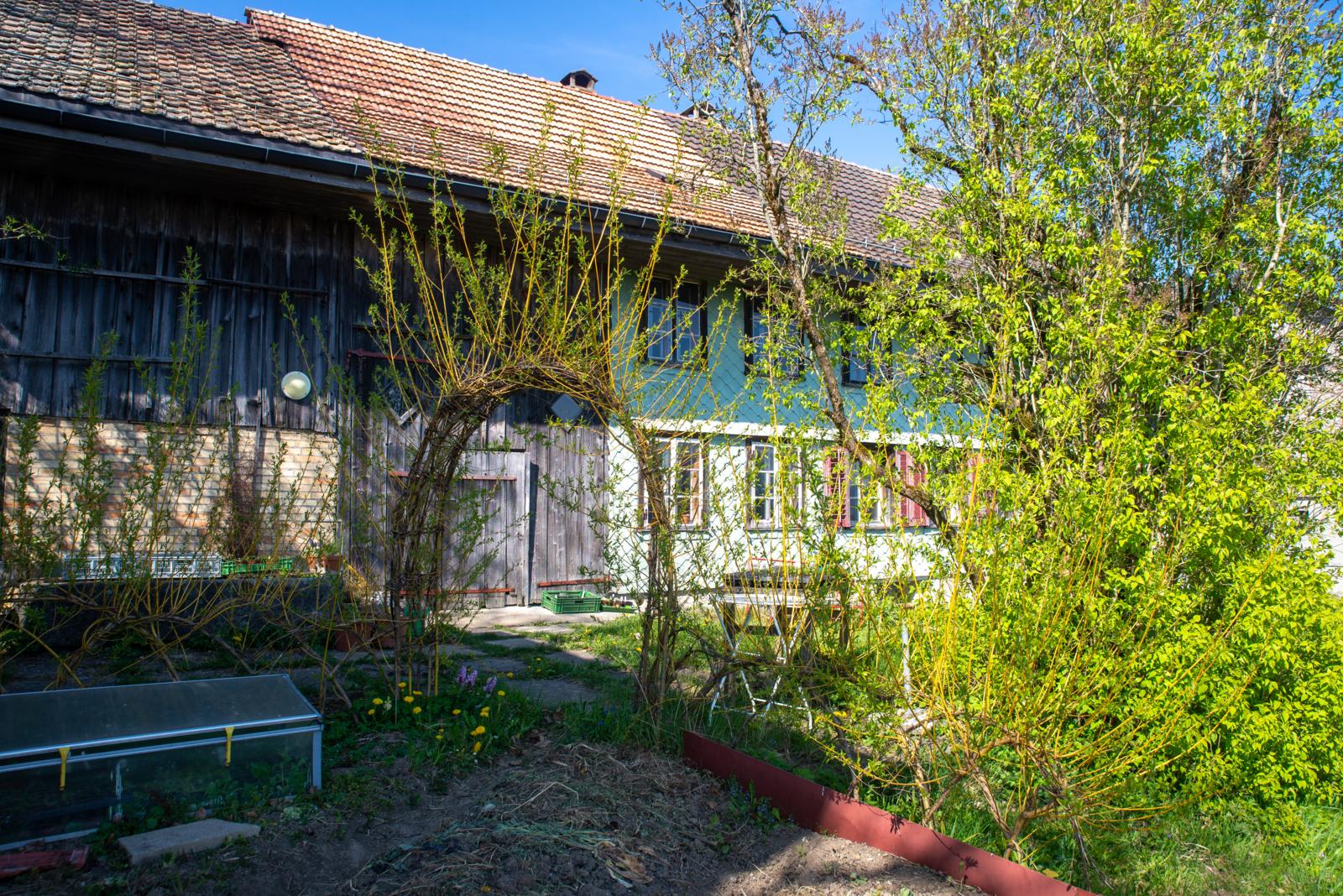 Auf dem Foto sieht man ein altes Bauernhaus mit Büschen im Vordergrund.