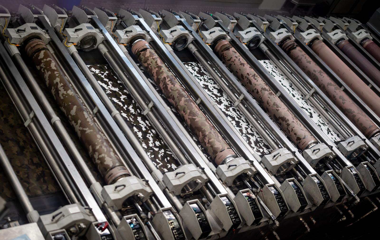 Durch eine Maschine mit mehreren Walzen läuft ein Stoff und wird mit Tarnmuster bedruckt.