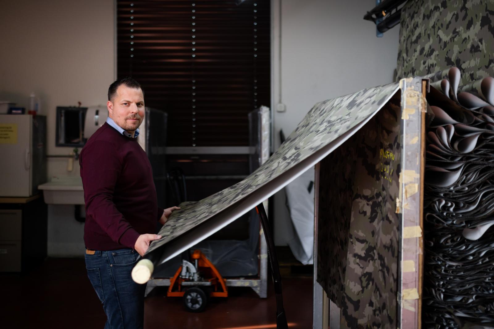 Ein Mann steht vor einem Rahmen, auf dem Armee-Stoff liegt.