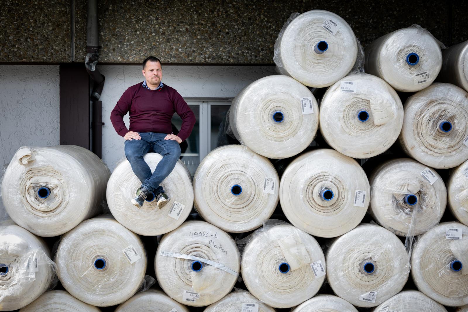 Ein Mann sitzt auf einem Ensemble grosser, aufeinandergestapelter Stoffballen.