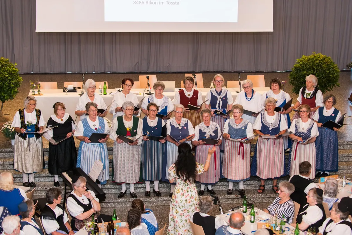 https-zueriost-ch-sites-default-files-elvis-media-2022-05-trachtentreffen-rikon-2022-12_preview-jpg Ein Chor gibt am Trachtenfest ein Lied zum Besten., Katharina Ruh stimmt ein Mitsinglied an., Elisabeth Comminot überreicht der Gemeindepräsidentin Regula Ehrismann einen Blumenstrauss., Zwei Oberländer Trachten: Links Cornelia Perret mit Festtagstracht und rechts Ursi Kündig mit einer Werktagstracht., Präsidentin Elisabeth Comminot hat den Anlass mitorganisiert., Anita Bachmann trägt eine Festtagstracht aus dem Zürcher Weinland., Bernadette Strassmann ist aus St. Gallen ins Tösstal gereist., Gertrud Held aus Wila trägt eine Tösstaler Werktagstracht., Margrit Solenthaler aus Trogen mit einer Tracht aus Appenzell Ausserrhoden.