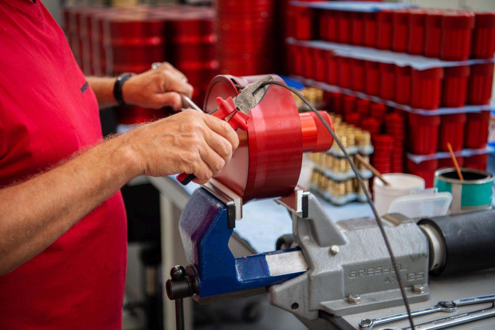 An einer Werkbank arbeitet eine Person an einem roten Werkstück.