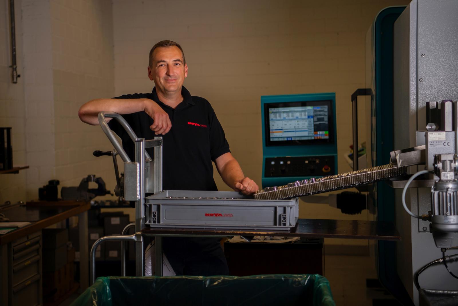 Ein Mann mit schwarzem Shirt steht an einer Maschine mit kurzem Förderband.