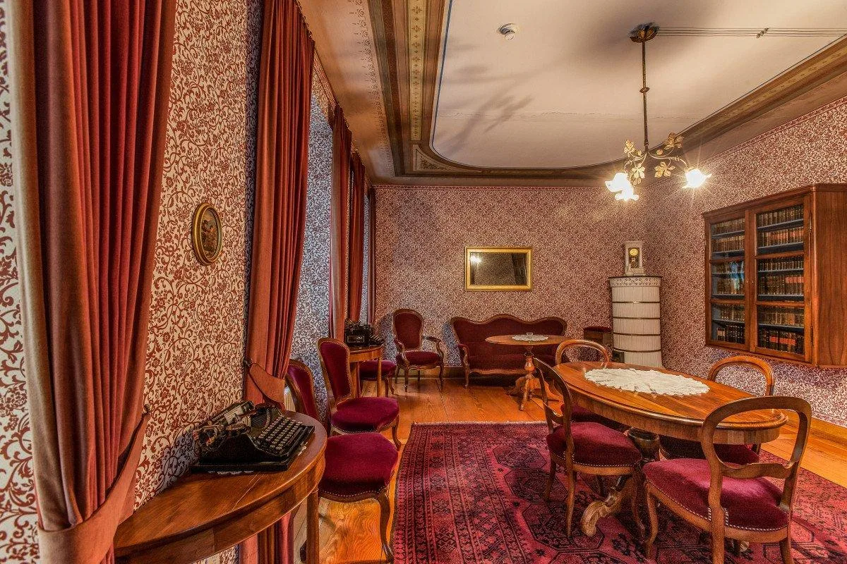 Man sieht den Damensalon im Gasthof Gyrenbad in Turbenthal. Man sieht ältere Tische und Stühle und hinten ein Kachelofen.