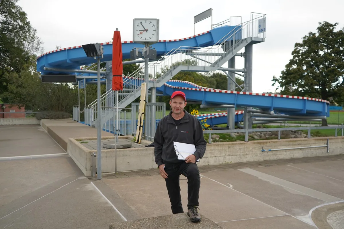 Ein Mann mit Basballcap vor einer Rutschbahn in einer Badeanstalt.