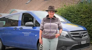 schulbustour-theres-k%c3%bcng-vor-bus_preview Schulbusfahrerin Theres Küng kennt die Strassen im Pirg auswendig., Der Schulweg führt an saftigen Wiesen, Schlaglöchern und Schafweiden vorbei., Dennoch: Theres Küng lässt sich nicht aus der Ruhe bringen.