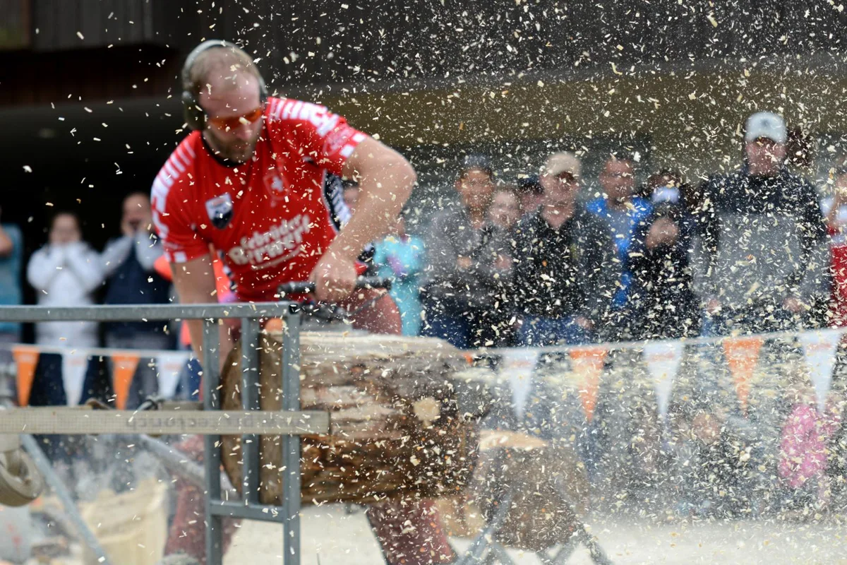 Schwitzend zeigten die starken Holzfäller ihr Können., Laut, lauter, Holzsymposium. Die Zuschauer ertrugen den Krach aus nächster Nähe., Der Anlass setzte sich zum Ziel, der Bevölkerung ..., ... den Umgang mit Holz näherzubringen., Die Veranstalter demonstrierten, was aus Holz entstehen und wie man es bearbeiten kann., Mit Äxten, Motorsägen und Kettensägen wurde gearbeitet., Es ging aber nicht nur um raue Krafteinwirkung, ..., sondern auch um Kreativität und filigrane Kunst.