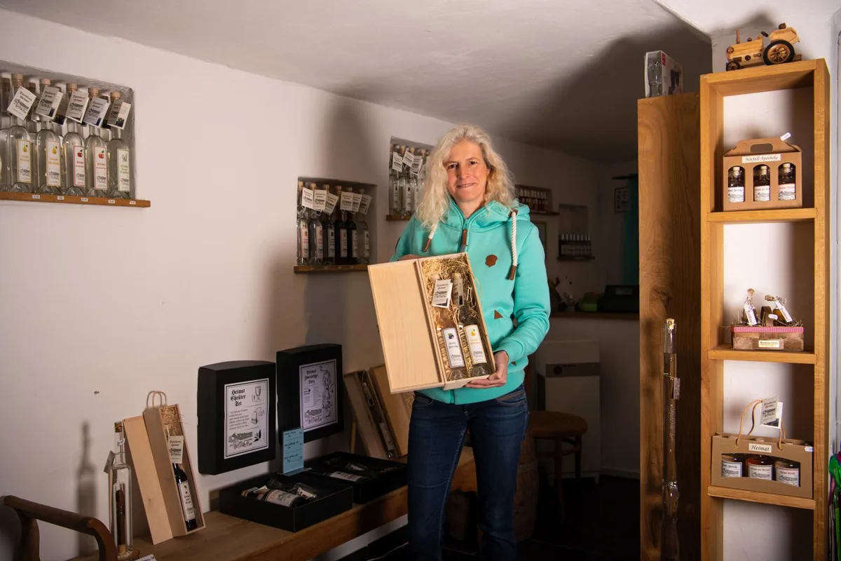 Auf dem Foto sieht man eine blonde Frau mit blauer Jacke, die eine Box gefüllt mit Schnapsflaschen in den Händen hält. 