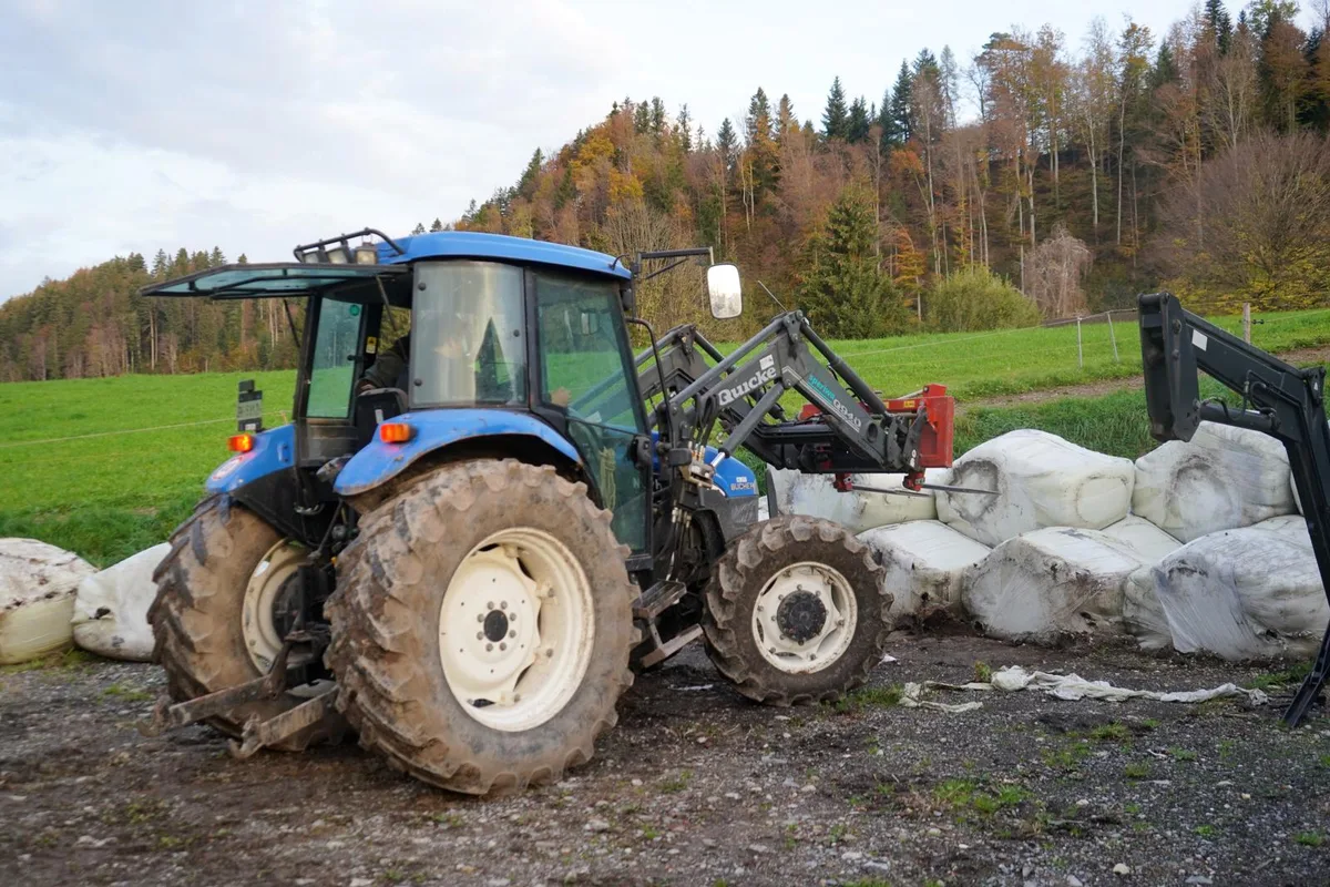 Auf dem Foto sieht man einen blauen Traktor, der von einem Mann und einem Jugendlichen bedient wird.