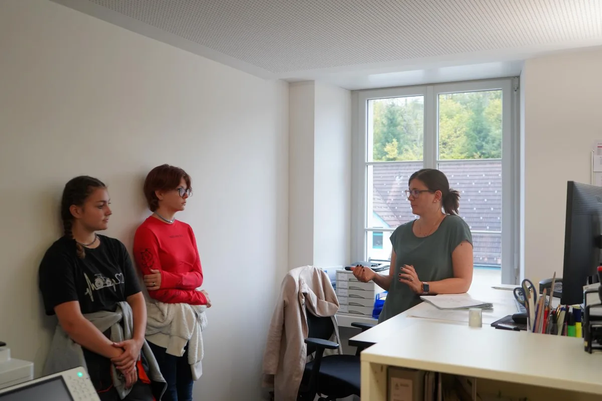 Auf dem Foto sieht man zwei Jugendliche und eine Frau in einem Büro. Letztere spricht mit den Jugendlichen.
