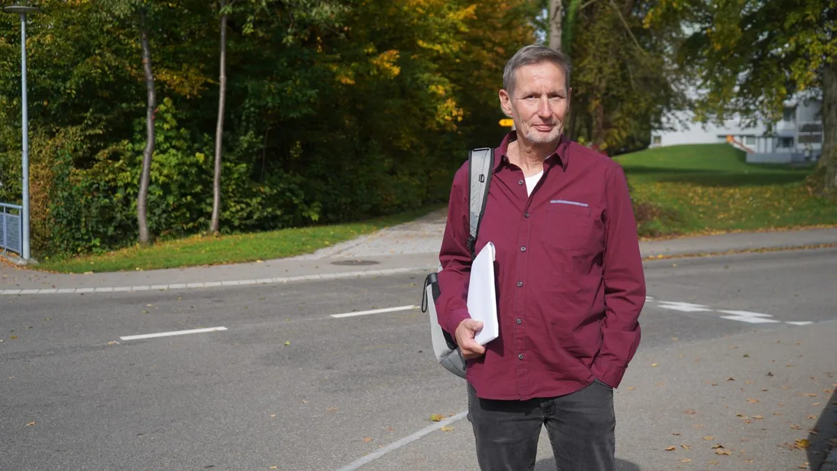 Auf dem Foto sieht man einen Mann mit weinrotem Pullover, der vor einem ehemaligen Fussgängerübergang steht.