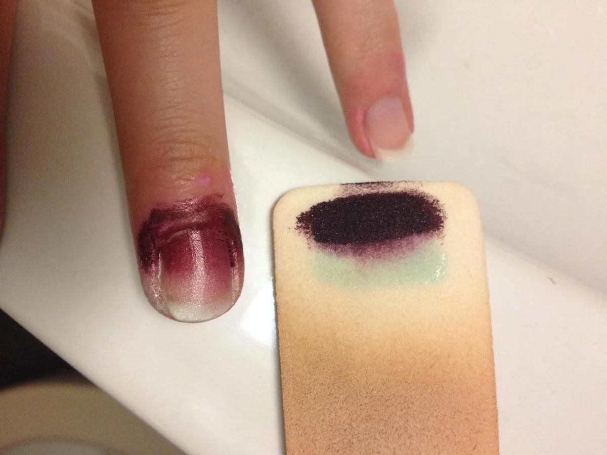 Ein möglichst tolles Design, möglichst einfach in der Anwendung - so sollte der perfekte Nagelschmuck sein. (Bild: Lea Chiapolini), Mit einer Silikonpaste werden die Teile des Nagels, die nicht mit Farbe in Berührung kommen sollten, abgedeckt. (Bild: Lea Chiapolini), Tropfenweise werden beim Water Marbling die Nagellacke in das Wasserglas geträufelt, sodass mehrere ineinander gelegte Ringe auf der Wasseroberfläche entstehen. (Bild: Lea Chiapolini), Mit einem Zahnstocher kann das Design noch weiter verfeinert werden. (Bild: Lea Chiapolini), Durch das Eintauchen des Fingers in das Wasser wird die Farbe auf den Nagel übertragen. (Bild: Lea Chiapolini), Das Ergebnis: eher enttäuschend. Die beiden Farben scheinen sich übereinander gelegt zu haben, sodass nur noch Violett zu sehen ist. (Bild: Lea Chiapolini), Bei der Ombré-Technik werden die Farben mithilfe eines Schwamms mehrere Male auf den Nagel aufgetupft. (Bild: Lea Chiapolini)