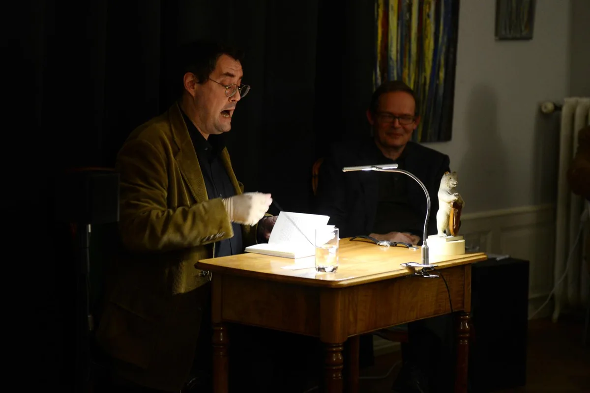 Autor Gion Mathias Cavelty (links) und Moderator Christoph Meister führen durch den Abend. Eine Nebenrolle kommt dem Harfe spielenden Bär zu. (Bild: Mirjam Müller) , Aus dem Publikum werden Fragen gestellt. (Bild: Mirjam Müller) , Beim anschliessenden Apéro können die Besucher den Autor besser kennen lernen. (Bild: Mirjam Müller) , Sein neuestes Werk mit «Gold» überzogen.(Bild: Mirjam Müller)