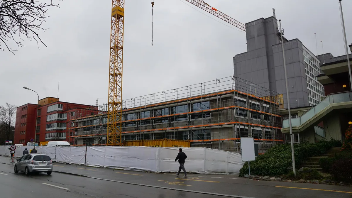Der L-förmige Zwischentrakt verbindet die Gebäude des Alters- und Spitexzentrums., Für den Rohbau benötigten die Arbeiter acht Monate., Im Zwischentrakt wird die neue Cafeteria gebaut., Der erste Erweiterungsbau (rechts) hat den Innenhof verkleinert, dafür wurde die Aussenanlage aufgewertet. , Stadtpräsident André Ingold bei seiner Ansprache., Sozialvorsteherin Jacqueline Hofer dankt den Anwesenden. , Bald wird das Essen serviert., Der «Promi-Tisch» mit Behördenvertretern.