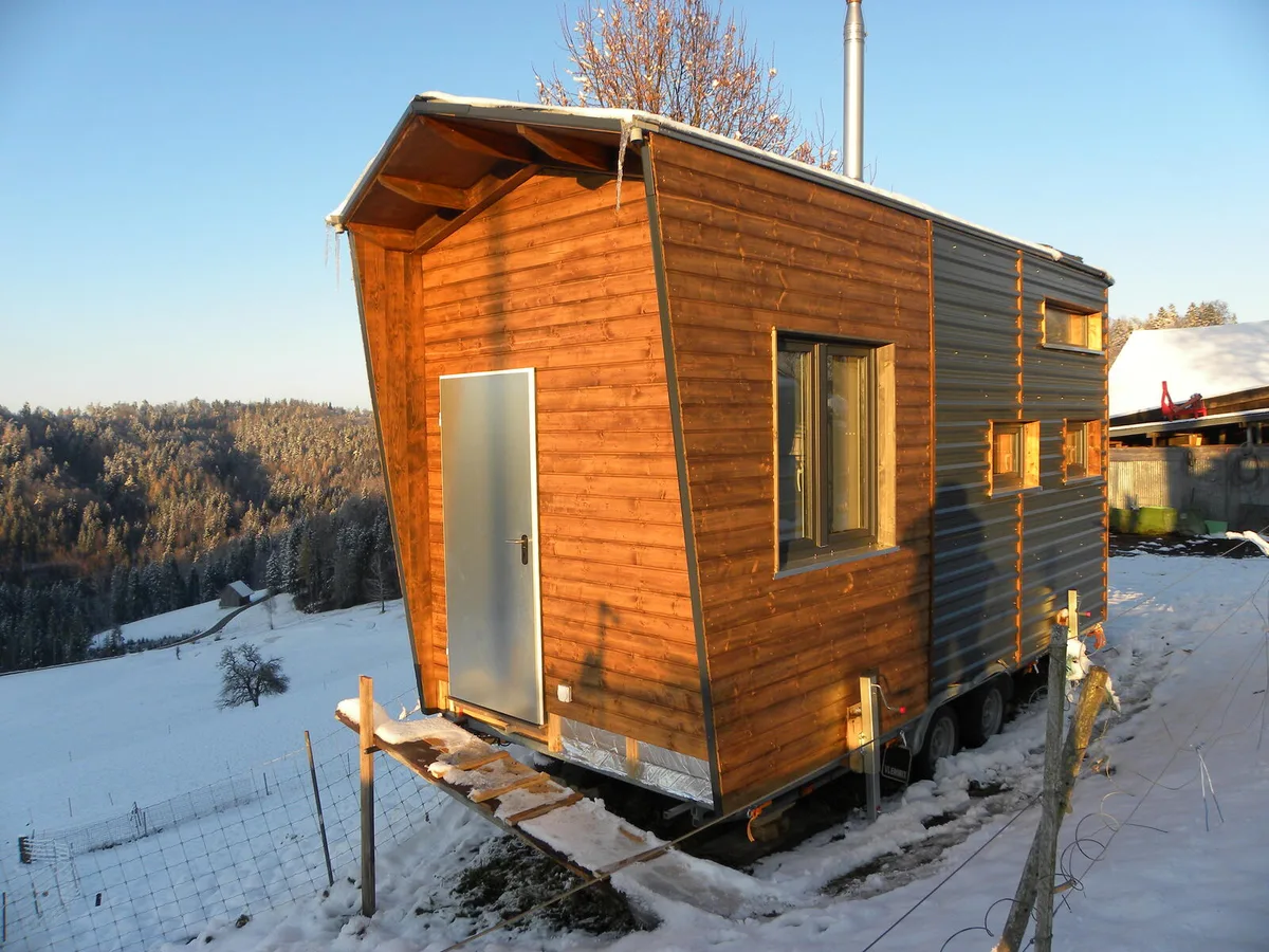 dscn6315 Die Abendsonne färbt das Tiny Hous in goldenen Glanz, während Eiszapfen an den Regenrinnen hängen., Das zum Verkauf stehend Tiny House mit Aussenwänden aus Holz und Metall., Michael Federer im Wohntrakt mit diversen technischen und anderen Raffinessen., Der Küchenbereich samt Badezimmer und der Schlafstätte oben., Die Ablage im Schlafbereich eignet sich auch als Büromöglichkeit.