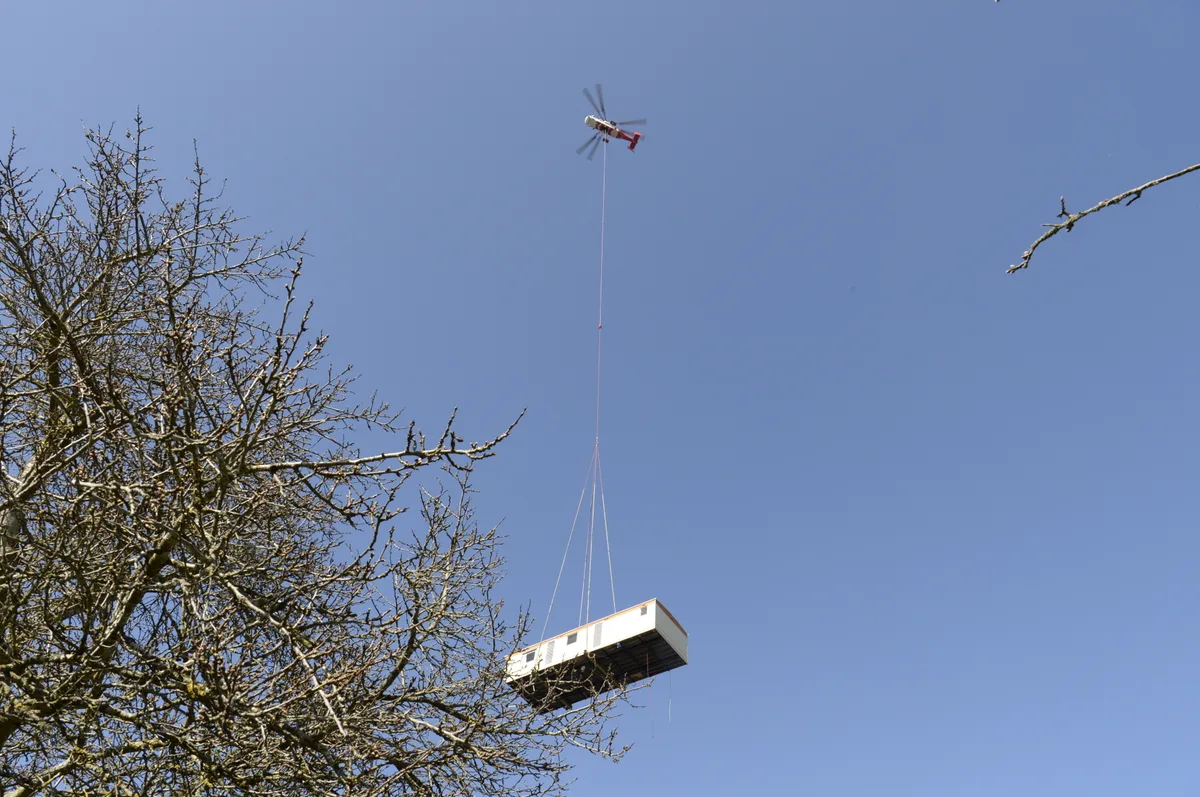 310321_campingplatz_mobilhome_weu_4 Die Platzierung des Mobilhomes erfolgte durch einen Helikopter., Ein Tieflader transportierte das Mobilhome zum Campingplatz in Wildberg., Dort wartete bereits ein Team mit dem Schwerlastenhelikopter., Das Mobilhome wurde auf die Höhe seinen künftigen Stellplatz transportiert, …, … wo es langsam Richtung Boden schwebte., Die Helfer hatten alle Hände voll zu tun, um das Mobilhome richtig zu platzieren., Präzisionsarbeit war gefragt.