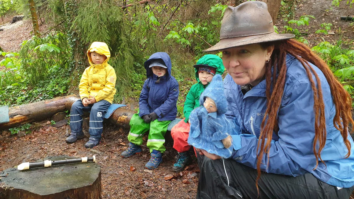 210521_waldspielgruppe_purzelwurzel_henne-issing_1 Cayan Biberstein mit der Handpuppe Anna Mae, die den Kindern nachdenkliche Geschichten nahebringt., Corinne Bachmann unterstützt beim Basteln eines Traumfängers., Gemeinsam im Inselkreis: In der Mitte Cayan Biberstein, rechts Corinne Bachmann., Draussen sein macht hungrig: Suppe, Brot und ein warmer Tee halten fit., Spielen mit Moos, mit Holz und allem was sonst noch da ist: Die Kinder werden kreativ., In den nächsten Wochen soll ein Traumfänger für jedes Kind entstehen. Gebastelt wird gemeinsam.