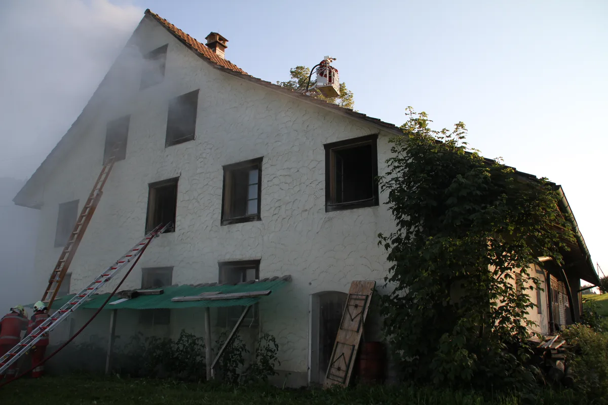 rauchschwaden_haengen_ueber_dem_anwesen Rauchentwicklung in einem Bauernhaus: Das war das Szenario der Sommerübung der Feuerwehr TWW., Das erste Fahrzeug erreicht den Brandübungsort., Das Tanklöschfahrzeug trifft ein., Die Drehleiter wird genutzt, um den landwirtschaftlichen Gebäudeteil zu schützen., Da die Tür verschlossen ist, kommt die Motorsäge zum Einsatz., Die ersten Feuerwehrleute betreten über die Fenster das Gebäude., Dies, um die Personen zu retten., Die Feuerwehrleute sind voll ausgerüstet mit Atemschutz., Eine schwerverletzte Person wurde geborgen und geht zur Erstversorgung., Die Mitglieder der Jugendfeuerwehr stellen sich als Opfer zur Verfügung., Erste Manöverkritik durch Einsatzleiter Stefan Baumgartner., Ausbildungschef Reto Gubler (rechts) im Gespräch., Gruppenbild nach der Übung.