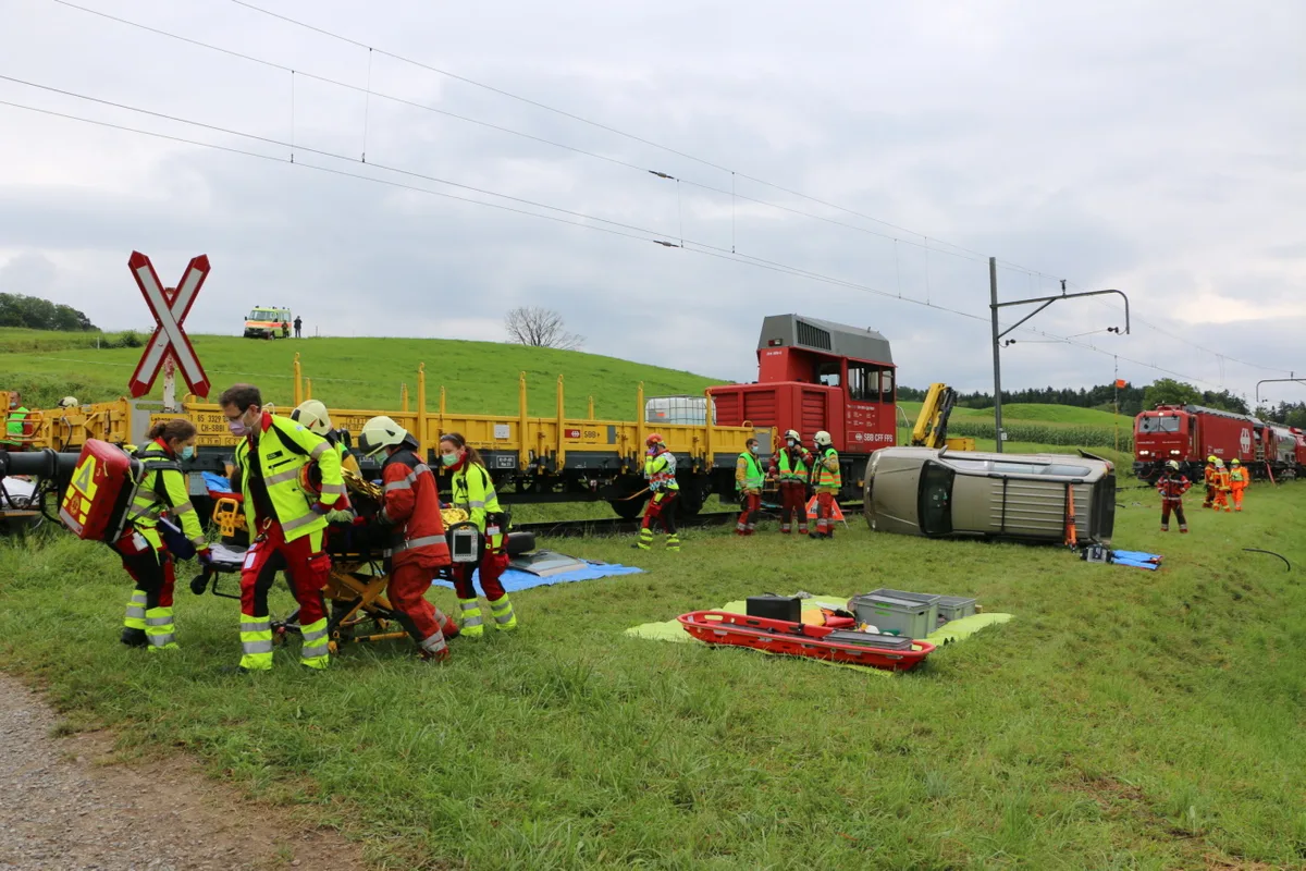 a_1_r_img_5112 Ein «Verletzter» aus einem der beiden Autos, die in den «Unfall» mit dem Bauzug verwickelt waren, wird abtransportiert., Die Feuerwehr öffnet eines der «Unfallautos», um einen Zugang zu den «verletzten» Passagieren zu schaffen., Eine Notärztin, ein Notarzt und eine Rettungssanitäterin widmen sich zwei «Patienten»., Ein «Verletzter» liegt erstversorgt zum Abtransport bereit., Und bald darauf läuft der Abtransport der «Patienten» ..., ... zu den bereitstehenden Rettungswagen.