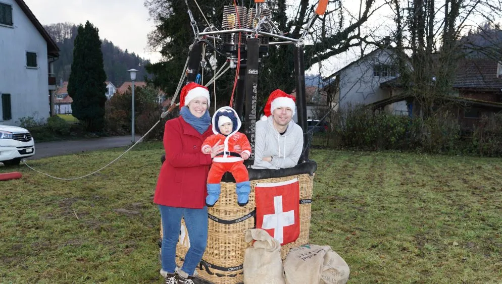 ballonfahrer_hugi_mit_frau_helen_und_sohn_2 Der Ballonfahrer Roman Hugi war gemeinsam mit seiner Frau Helen und Sohn Alex zu Besuch bei der Primarschule Hohmatt., Die Kinder durften sich über Chlaussäcke freuen, die Hugi vor Ort verteilte., Zum Schluss flog der Ballon los – zur Freude der Anwesenden., Allerdings wurde es keine lange Fahrt., Hugi landete den Ballon bereits beim Schützenhaus wieder., Dort wurde der Ballon sorgsam zusammengelegt und verstaut.