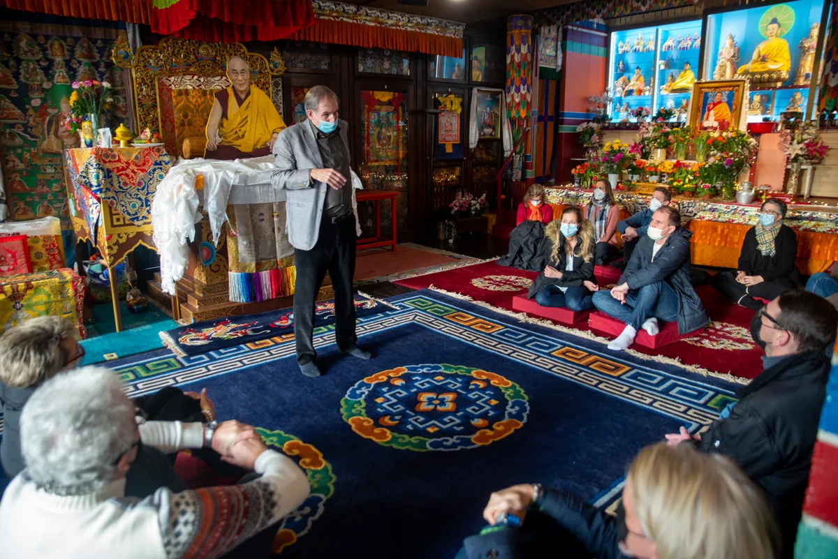 Frauen und Männer sitzen im Gebetsraum des klösterlichen Tibet Instituts. Im Hintergrund ist der Dalai Lama in Lebensgrösse zu sehen.