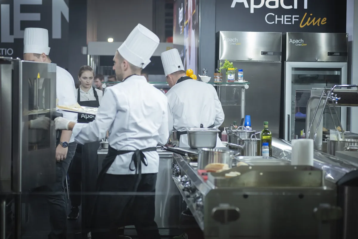 Mehrere Köche mit weissen Kochmützen arbeiten geschäftig in einer Restaurantküche.