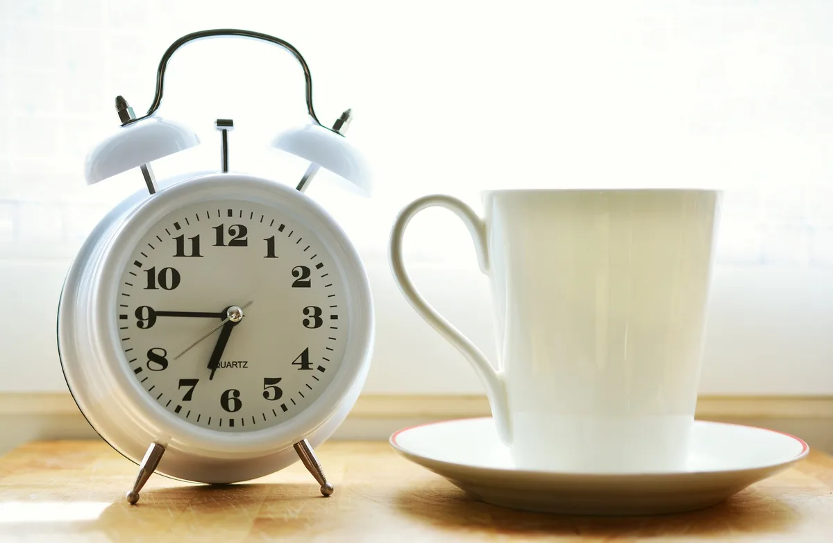 Ein weisser altmodischer Wecker und rechts davon eine weisse Kaffeetasse.