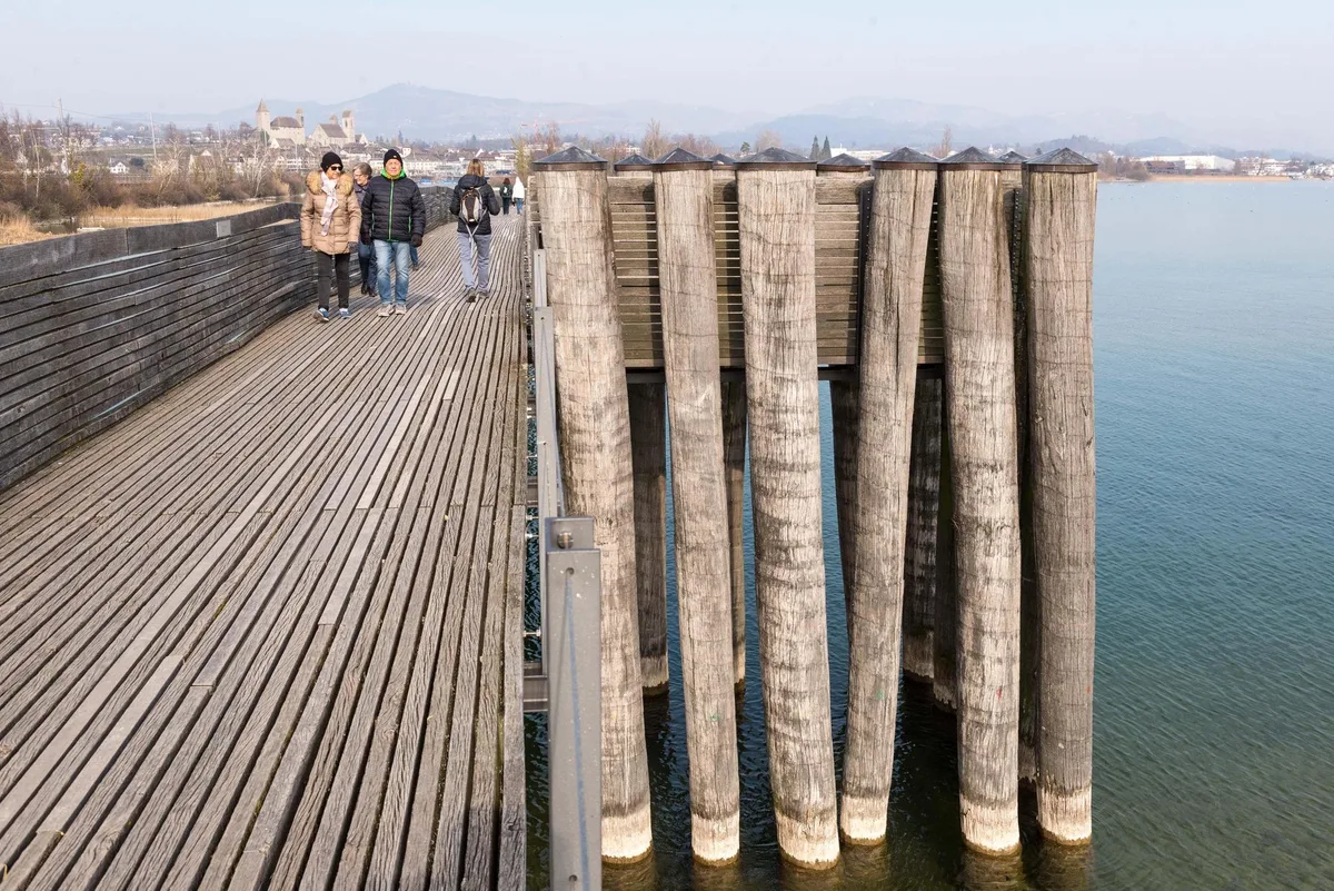 Mehrere Personen laufen auf einem Holzsteg in Richtung des Fotografen.