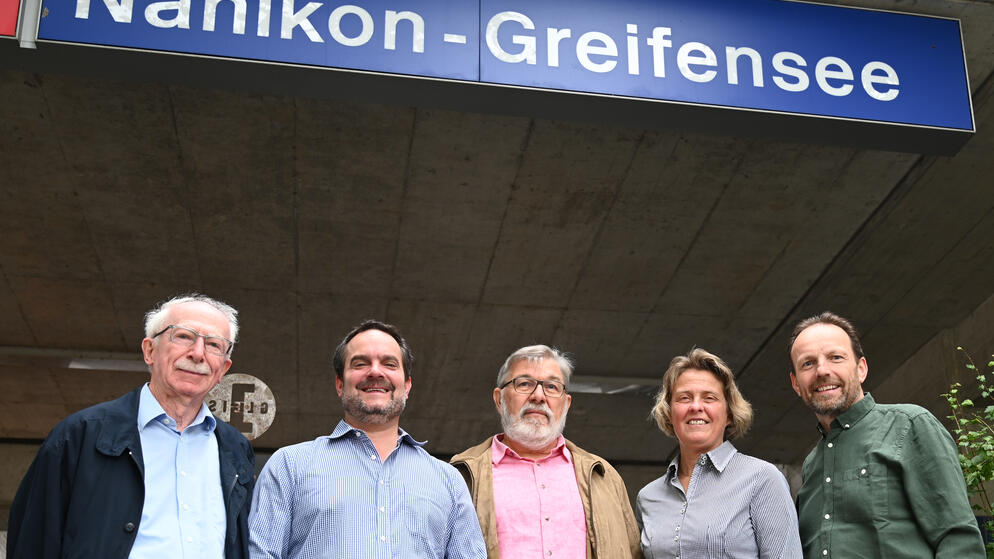 Vier Männer und eine Frau unter dem Bahnhofsschriftzug "Nänikon-Greifensee". Die Männer tragen Schnäuze.