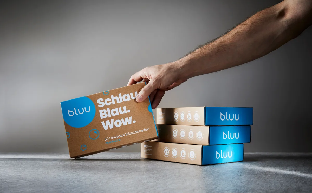 Eine Packung bluu-Waschstreifen wird von einer Hand ins Bild gereicht. 