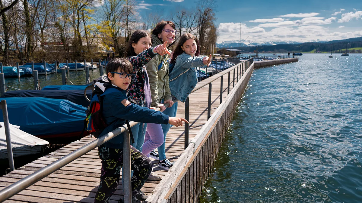 Mama Annette und die drei Kinder stehen in Niederuster auf dem Schiffssteg am Greifensee und zeigen auf irgendetwas in der Ferne. 
