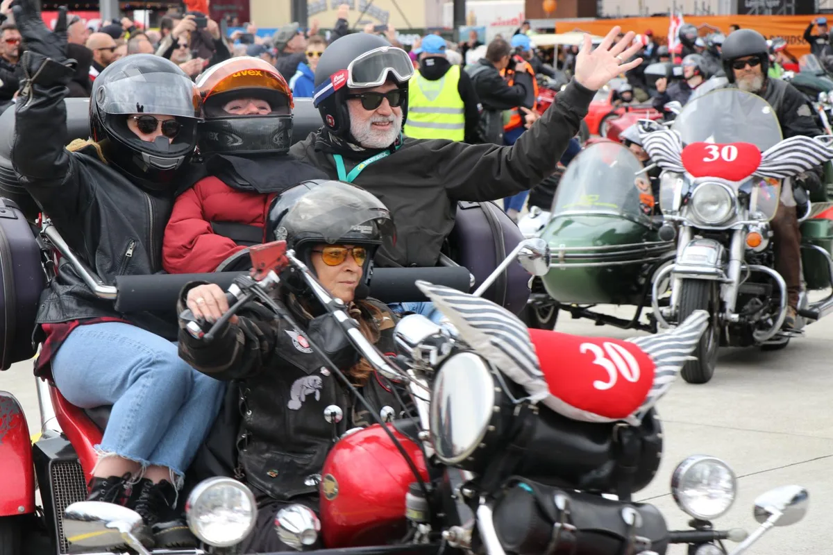 Mehrere Trikes starten ihre Ausfahrt -  mit vielen Menschen mit Helm. Eine bunte Szenerie.