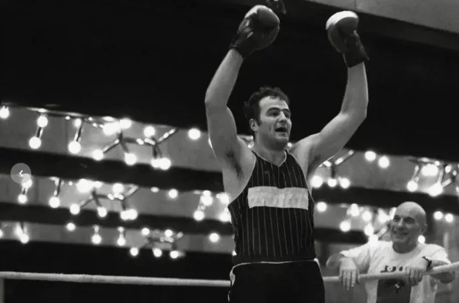 Schwarz-weiss Foto mit einem Mann mit Boxhandschuhen. Der Ringrichter hebt den Arm des Mannes zum Zeichen dafür, dass dieser den Kampf gewonnen hat.