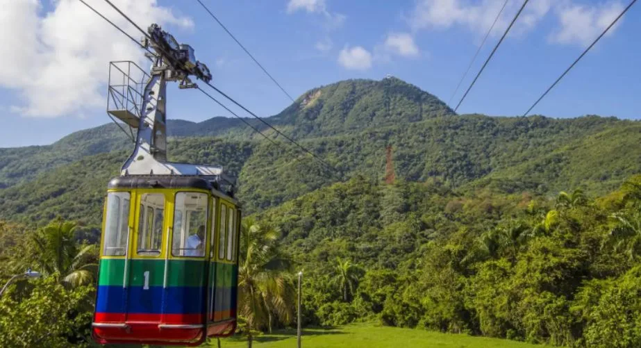 Eine bunt angemalte Seilbahn. Im Hintergrund ein grüner Berg auf den diese zu fahren scheint.