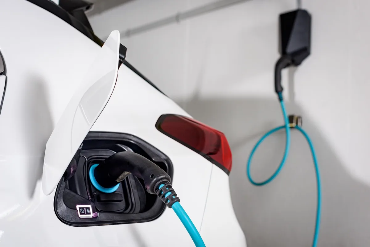 Zu sehen ist eine Ladestation für Elektroautos. Ein weisses Auto wird gerade geladen. Der Strom kommt von einer Ladestation via Kabel zur Steckdose am Auto.