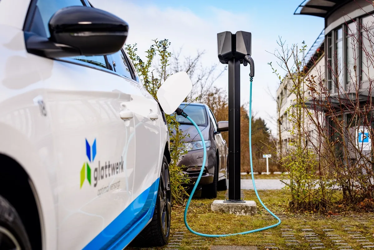 Eine Ladestation, die auf einem Ständer draussen montiert ist, lädt gerade ein Auto auf und ist mit diesem über ein Kabel verbunden.
