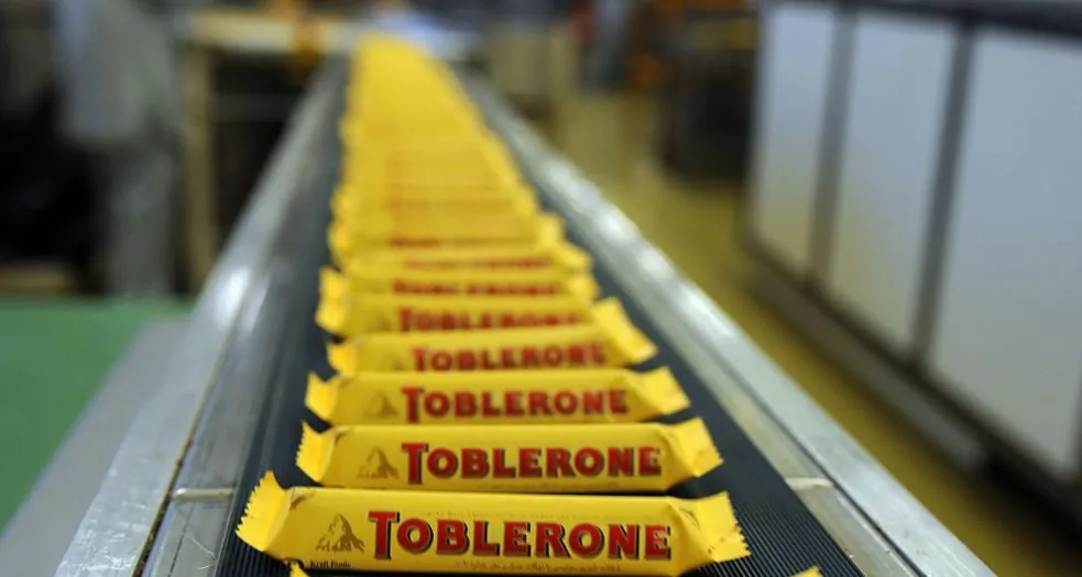 Zahlreiche Toblerone-Schokoladen laufen über ein Produktionsband. Sie ist in einer gelben Verpackung mit rot Aufschrift.