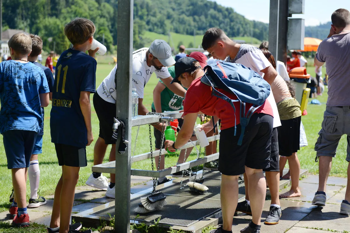 Auf dem Foto sieht man Kinder in Fussballerkleidung, die ihre Wasserflaschen füllen.