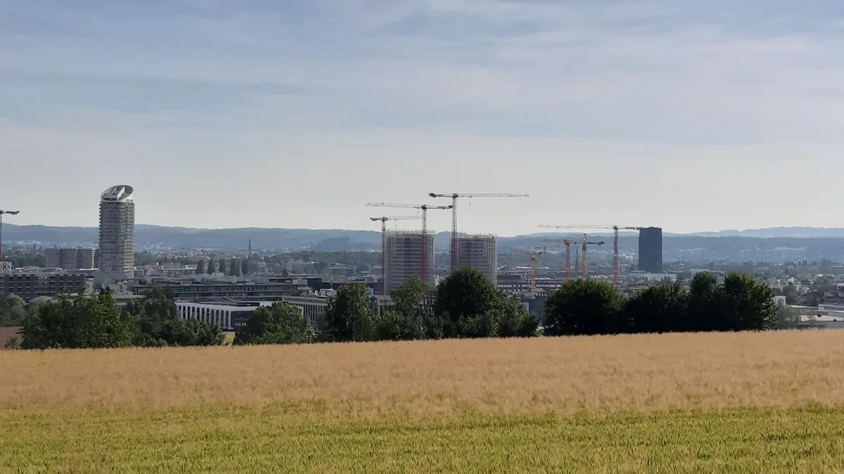 Blick über ein Feld auf das Quartier Hochbord mit dem Jabee-Tower und der Baustelle Three Point.