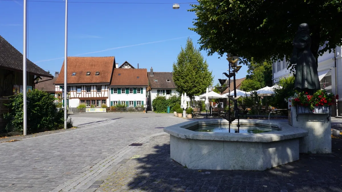 Im Vordergrund ist der Dorfbrunnen in Wangen zu sehen. Links eine Strasse mit Pflastersteinen. Im Hintergrund alte Fachwerkhäuser. 